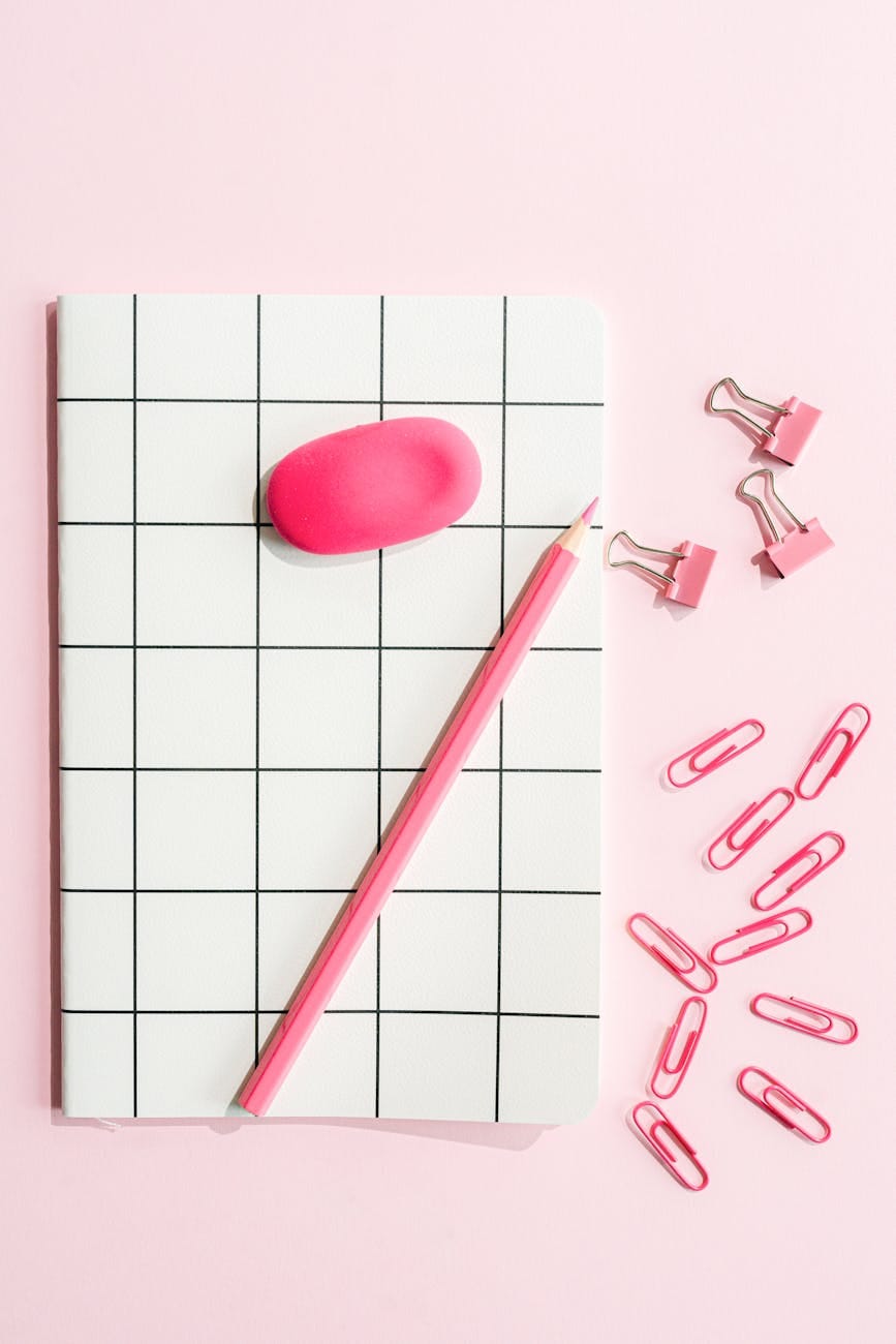 black and white notebook and pink pencil on pink background