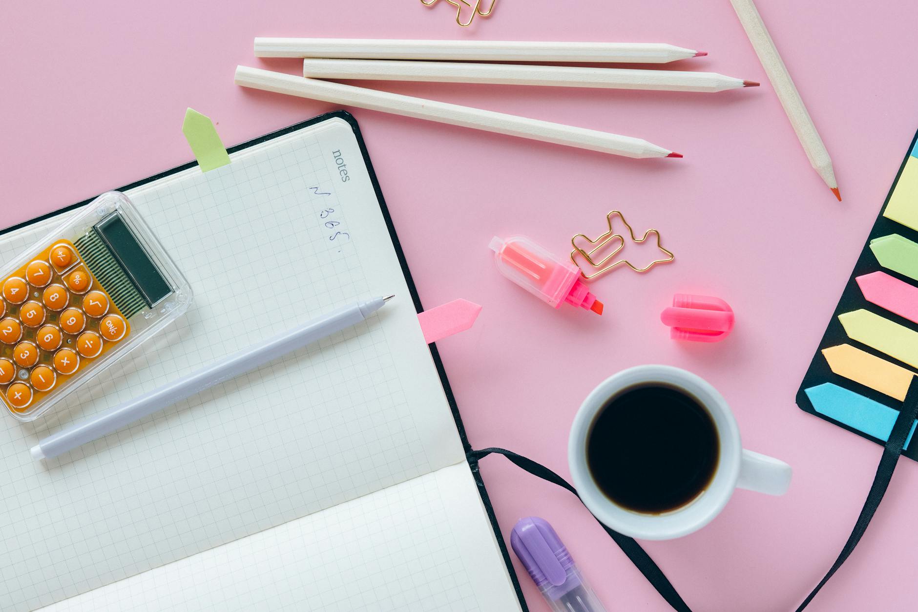 pink pen on white notebook beside white ceramic mug