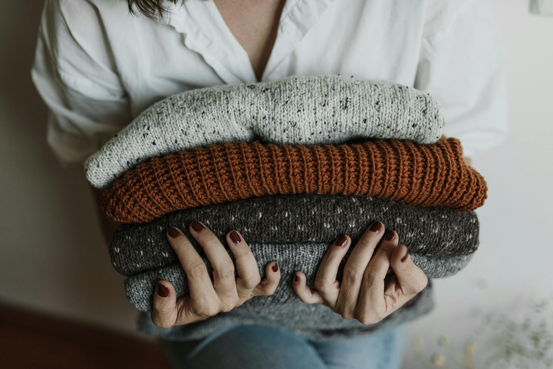 a close up shot of a person holding a stack of folded knitted fabrics