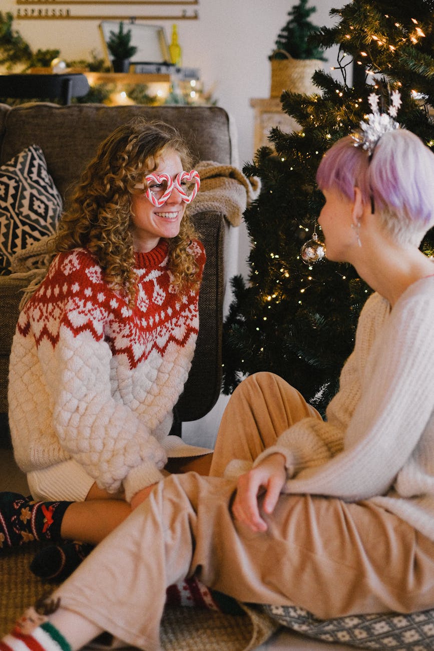 smiling women in christmas sweaters sitting on floor