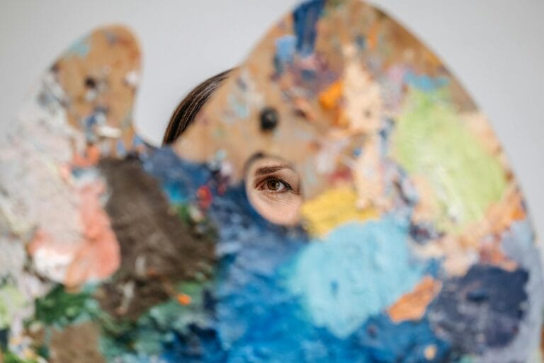 close up of woman looking through a hole in a palette with paint