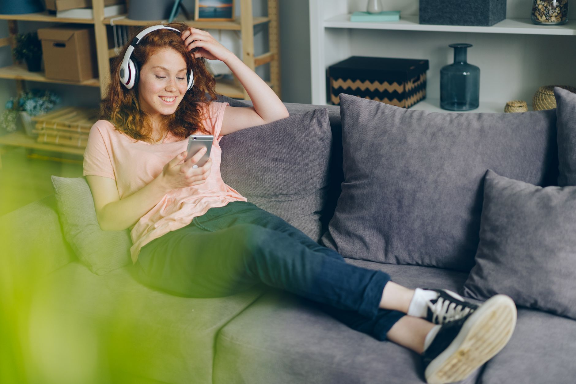 a woman with headphones sitting on a sofa and looking at her phone